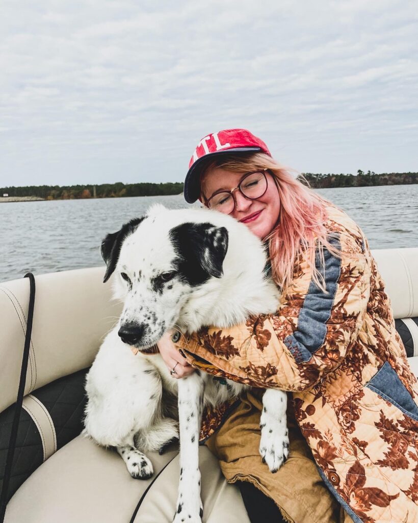 A woman hugs her dog on a boat, water visible behind them.